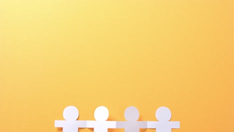 Close-up-of-people-holding-hands-made-of-white-paper-on-yellow-background-with-copy-space