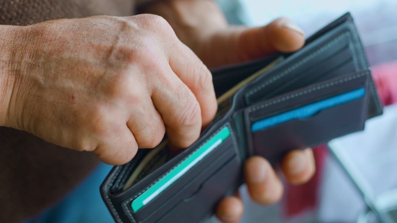 Nærbillede af en gammel mands hænder, der lægger dollarsedler i sin pung.