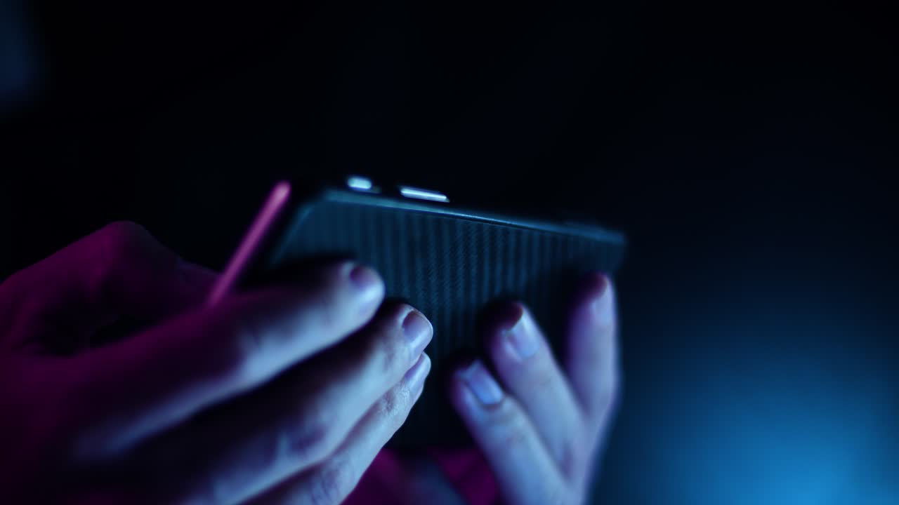 Thumb scrolling on a smartphone in landscape close up in a dark room with purple and blue lighting