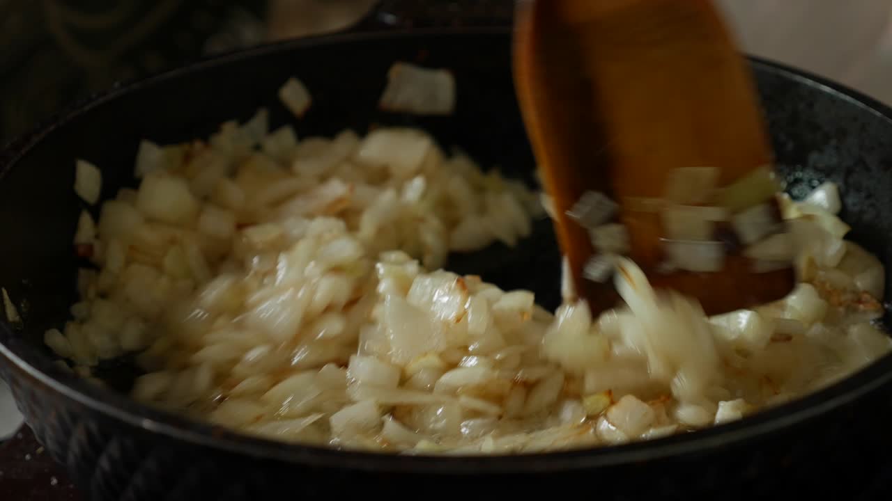 Frying onions in a pan with oil. Stir onion in skillet with wooden spatula