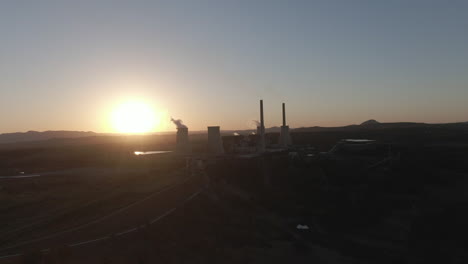 Aerial:-Drone-wide-shot-circling-a-power-station-as-the-sun-sets-behind-the-chimneys,-in-New-South-Wales,-Australia