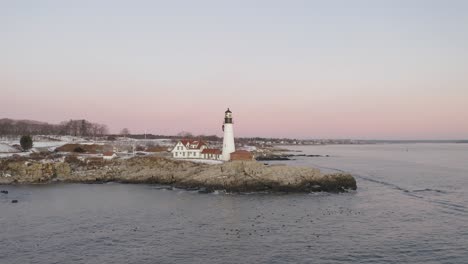 Sea-ducks-floating-below-Portland-Head-Light,-winter-sunrise-STATIONARY-AERIAL