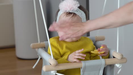 grandmother wearing bow on small baby head sitting doorway swing and playing with silicon flower toy smiling