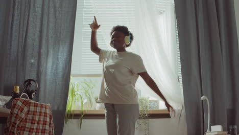 happy african american woman in headphones dancing at home