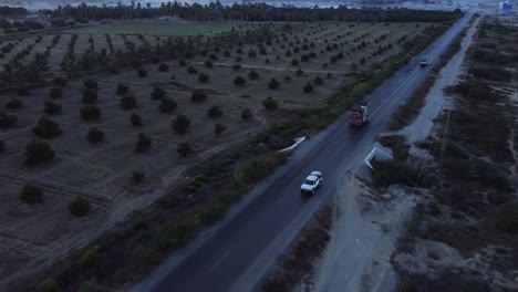 aerial drone backward moving shot over cars and lorries driving along rcd road with farmland on both sides of baluchistan during evening time