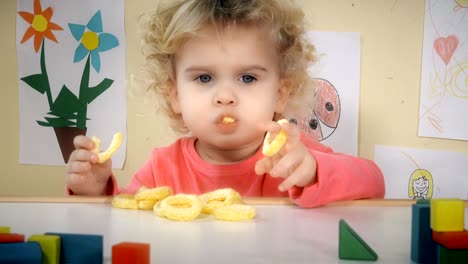 niño hambriento comiendo patatas fritas de maíz sentado cerca de la mesa en su habitación