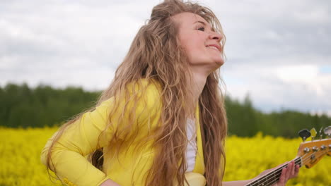 movimiento manual de la cámara siguiendo al guitarrista bailando. una hermosa chica con una chaqueta amarilla toca una guitarra en un campo de colza.