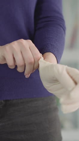 mujer se pone un guante de goma estéril en la mano preparándose para un procedimiento médico. ama de casa usa guantes desechables cuidando la higiene personal de cerca