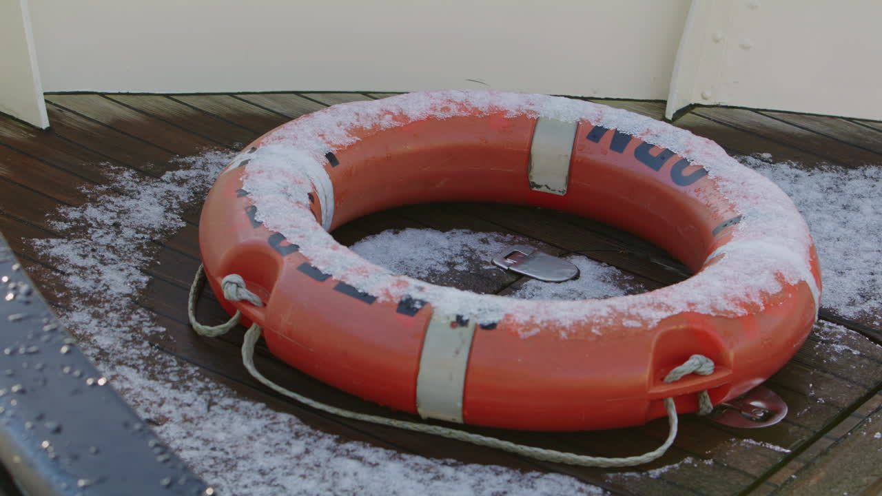 Close-up of a weathered lifebuoy resting on a wooden deck with light frost, symbolizing safety, rescue and maritime protection in cold winter conditions