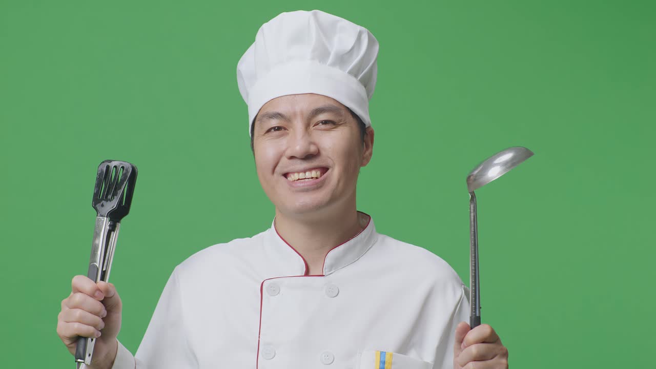 Close Up Of Asian Man Chef Smiling And Showing Tongs And Ladle To Camera While Standing In The Green Screen Background Studio
