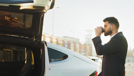un hombre de negocios disfrutando de café cerca de un coche eléctrico