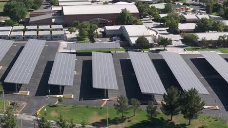 Vista-Aérea-Volando-Sobre-Paneles-Solares-Que-Cubren-El-Estacionamiento-Del-Campus-De-La-Escuela-Secundaria-En-Un-Día-Soleado