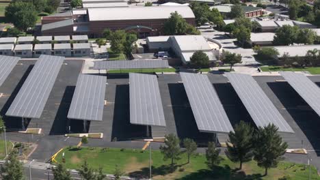 aerial view flying over solar panels covering high school campus parking lot on bright sunny day