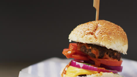 video close up of cheeseburger in burger bun with wooden skewer, on grey background with copy space