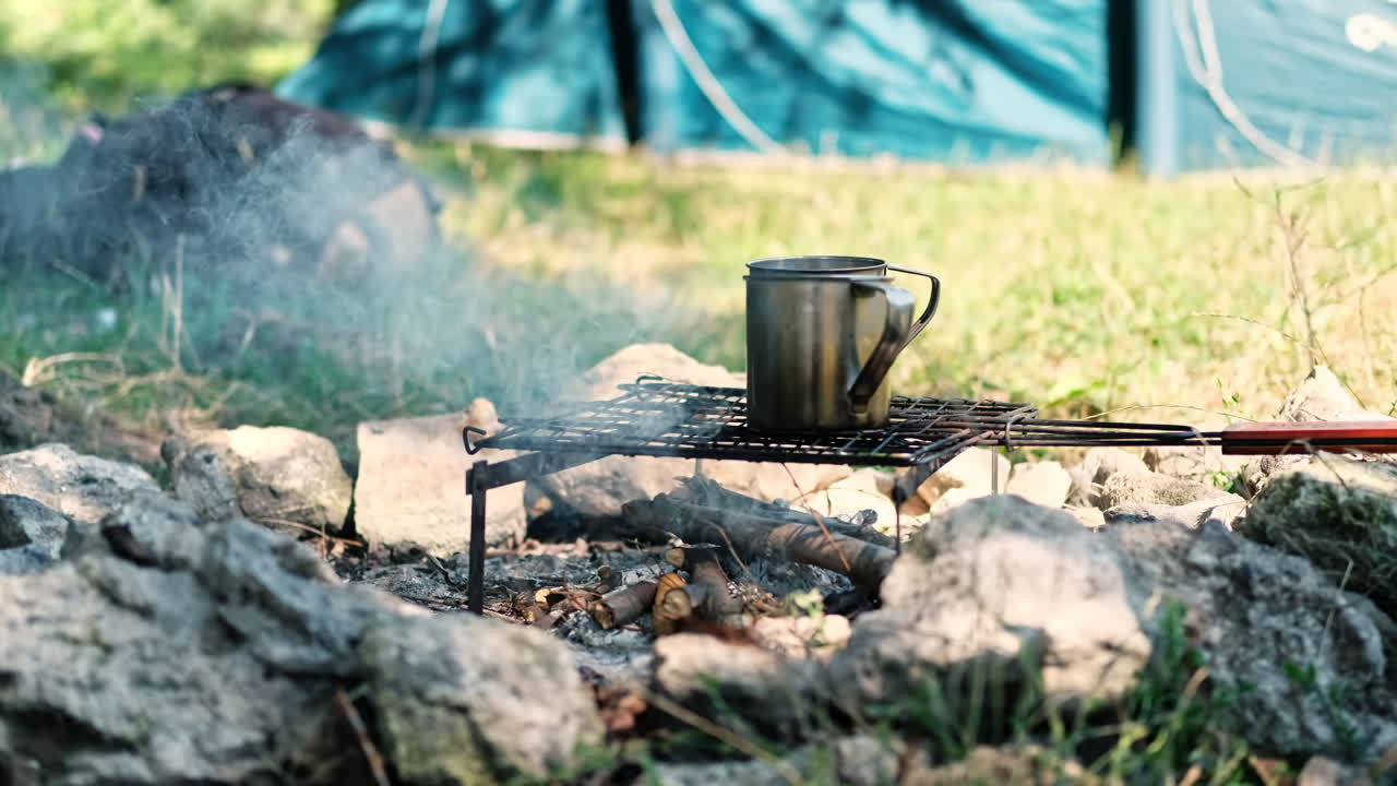 Water in two tin mugs is boiling on a grill grid above the campfire. Preparing coffee