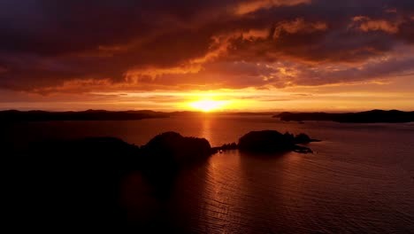 Hermosa-Puesta-De-Sol-Sobre-El-Mar-En-La-Isla-De-Poroporo,-Bahía-De-Islas-En-Nueva-Zelanda---Retroceso-Aéreo