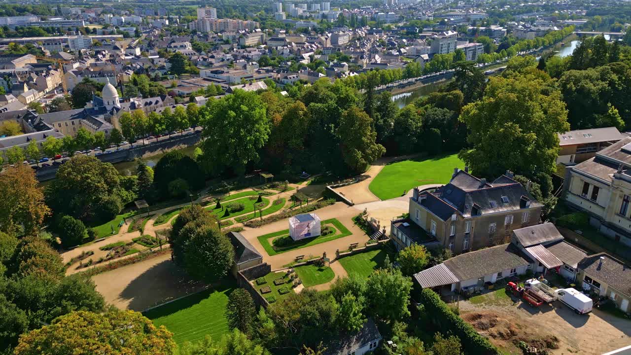 Drone shot flying over Jardin de la Perrine in Laval, showing the rose garden, pathways, and surrounding cityscape along the Mayenne River under clear skies