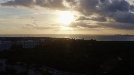 Langsame,-Rechts-Fahrende-Luftdrohnenaufnahme-Eines-Atemberaubenden-Gelb-goldenen-Ozeansonnenuntergangs-Mit-Tropischem-Grün-Unten-Vom-Crandon-Park-In-Key-Biscayne-Außerhalb-Von-Miami,-Florida,-An-Einem-Warmen,-Sonnigen-Sommerabend