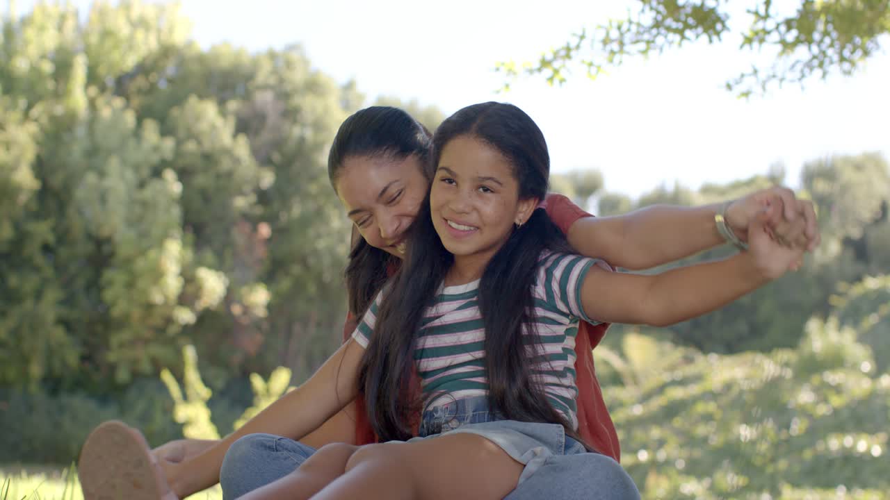 Madre afroamericana apoyando y levantando a una niña que finge volar en el parque mientras juega.