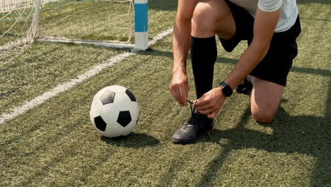 young football player tying his shoes on a street football pitch