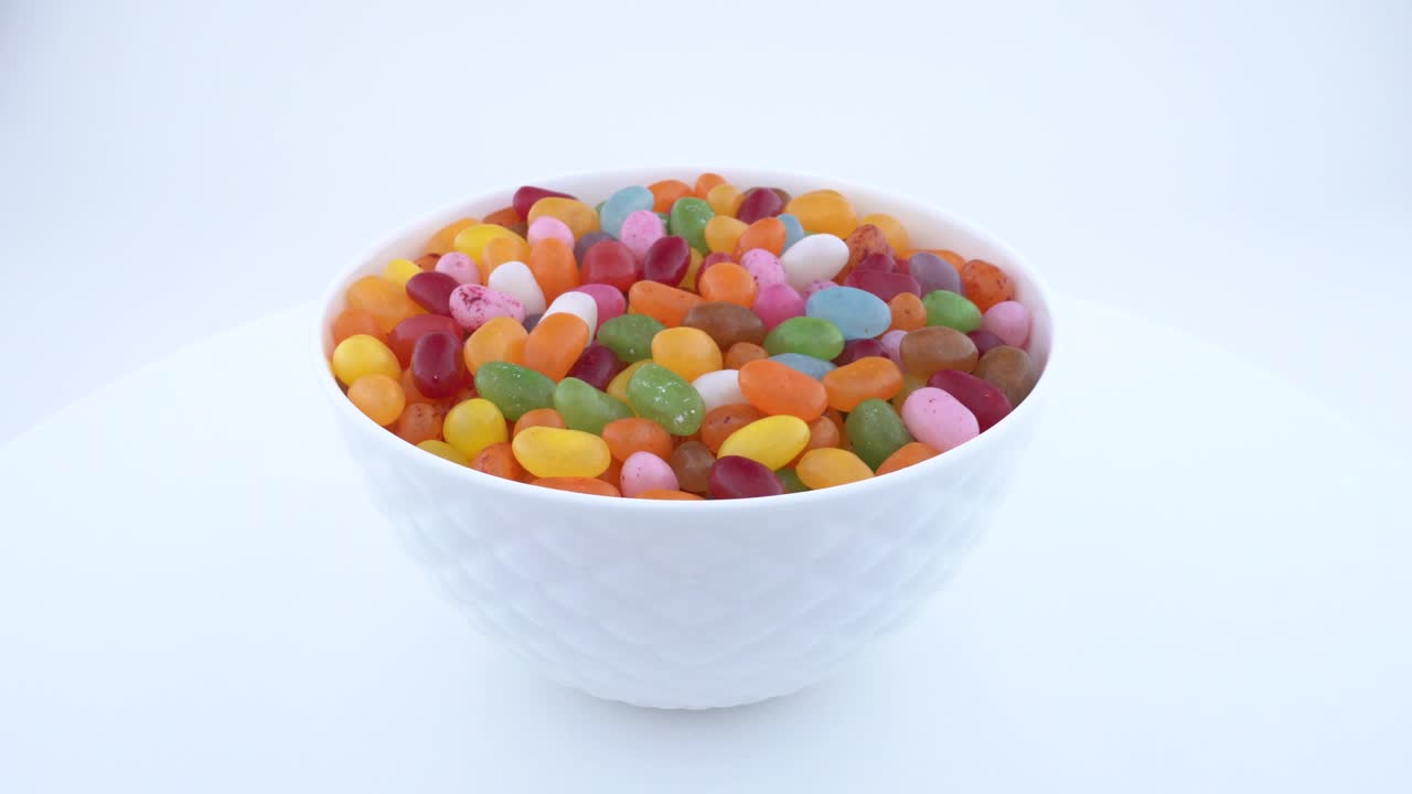pila de pequeños dulces de jalea de azúcar en forma de frijol. girando en un cuenco blanco en la mesa de giro. aislado.