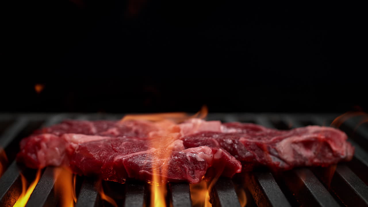 bistec de carne cayendo sobre la parrilla de carbón en el fondo negro, estallido de fuego desde debajo de la parrillas en cámara lenta