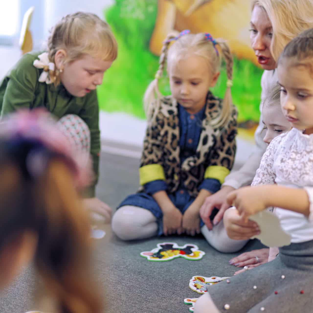 Little boys and girls play on floor at school. Children are sitting in a circle on a carpet with their teacher and study playing with colored cards. Educational process.