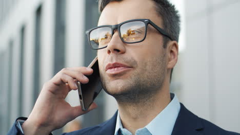 vista de cerca del hombre de negocios con gafas hablando por teléfono en la calle