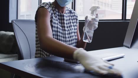 african american woman wearing face mask and gloves santitizing her workstation