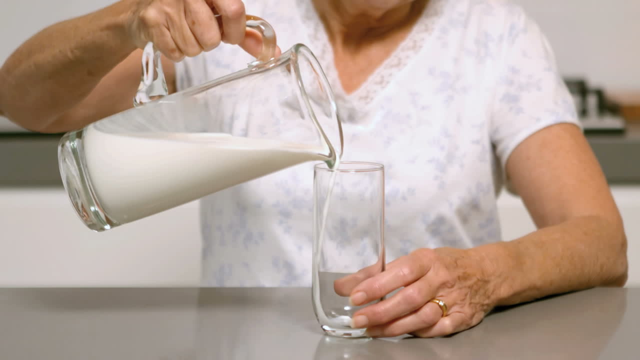 mujer vertiendo un vaso de leche en la cocina