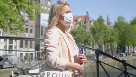 charming woman wearing mask, waiting for someone at the bridge over amsterdam canal in netherlands - medium shot