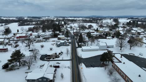 landing drone shot showing main street of suburban neighborhood in winter snow