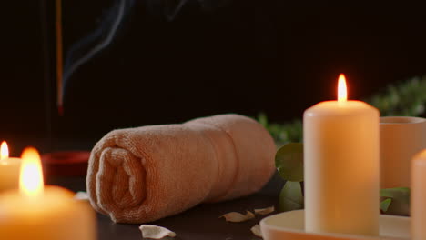 still life of lit candles with green plant incense stick and soft towels against dark background as part of relaxing spa day decor 1