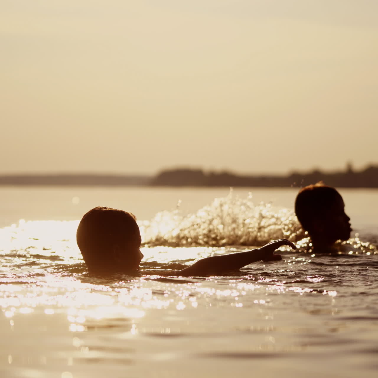 Little kids are playing in water and making splash; Children are swimming in lake or river and having fun with drops; Two brothers rollick at sunset. Monochrome video. Side view.