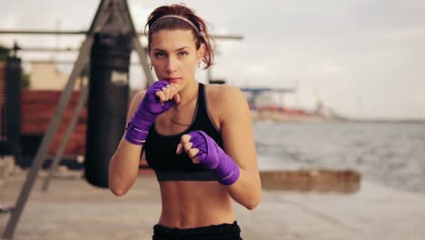 slow motion shot: young woman shadowboxing with her hands wrapped in purple boxing tapes looking in the camera. beautiful female