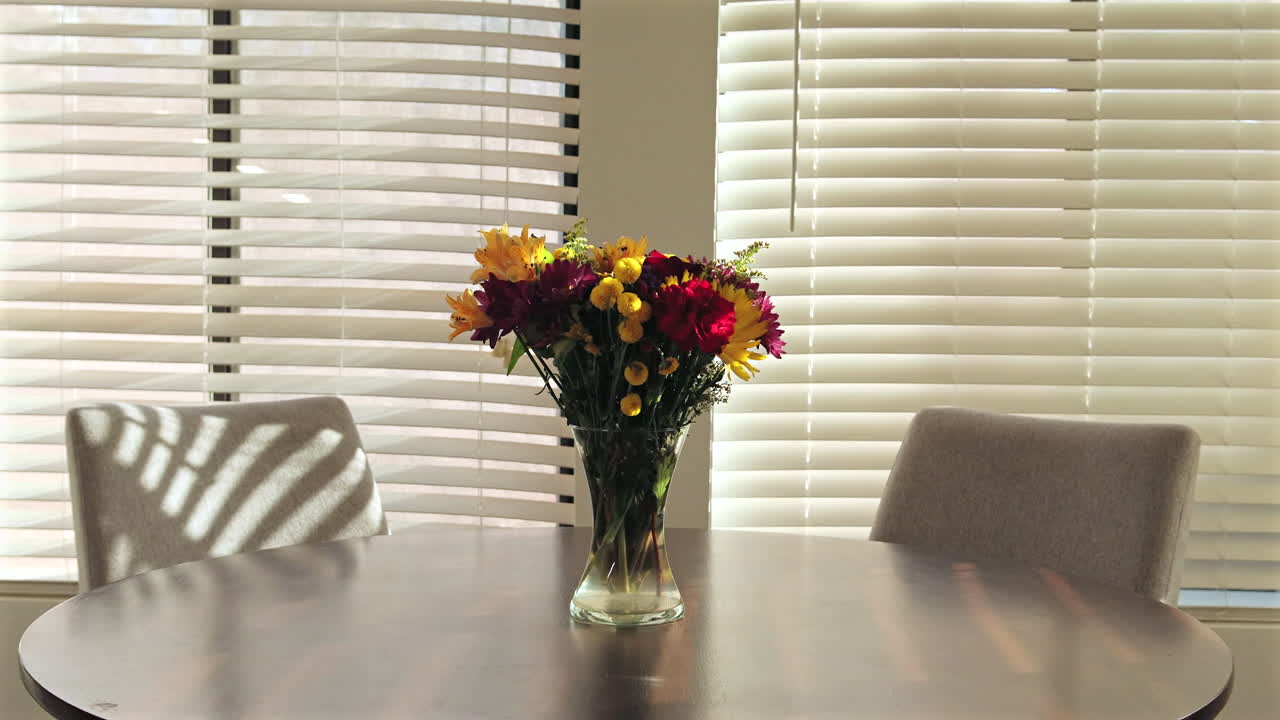 Bright sunlight illuminates a vase of colorful flowers on a round table, creating a warm atmosphere
