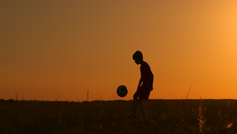 Ein-Junger-Fußballspieler-Trainiert-Mit-Einem-Ball,-Der-An-Seinem-Bein-Hängt,-Bei-Sonnenuntergang-In-Zeitlupe-Während-Der-Goldenen-Stunde-Auf-Dem-Feld-Bis-Zum-Sonnenuntergang.-Training-Von-Der-Dämmerung-Bis-Zum-Morgengrauen.-Konzeptweg-Zum-Erfolg