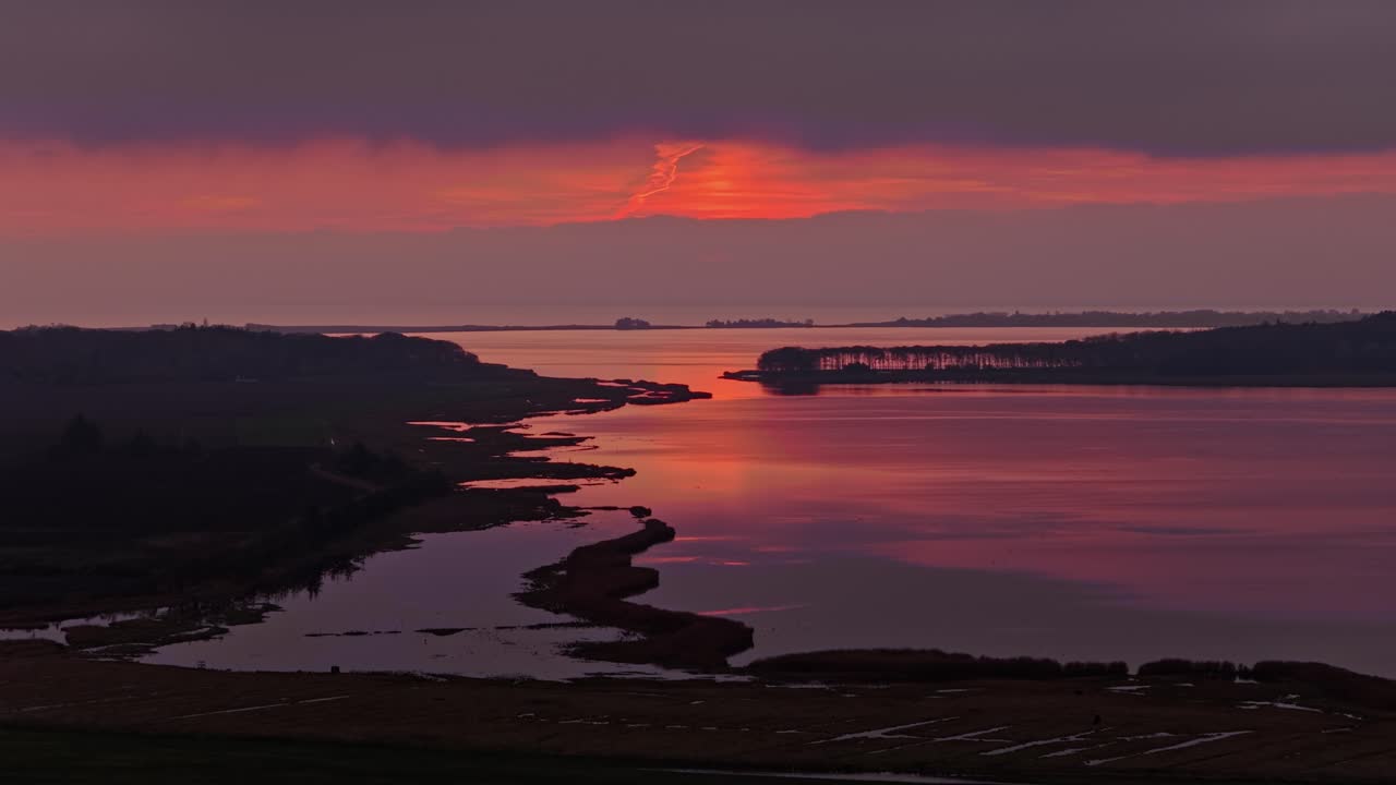 Smooth forward movement across tranquil water toward a vivid red and orange sunset with dark trees and islands. Peaceful nordic evening atmosphere