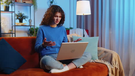Angry displeased upset young woman using laptop netbook receiving bad news sitting on home sofa