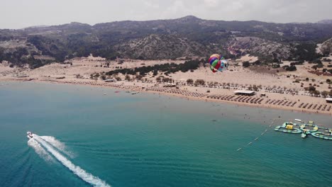 Parapente-Turístico-Con-Paracaídas-Colorido-Remolcado-Por-Lancha-Rápida-En-El-Mar-Azul-En-Un-Día-De-Verano-En-La-Isla-De-Rodas,-Grecia