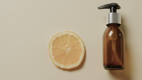close up of glass bottle with pump, lemon slice and copy space on beige background