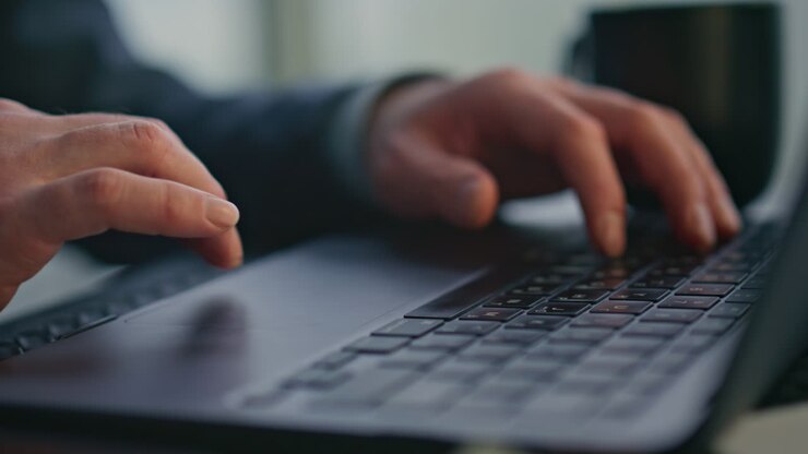 Nahaufnahme: Unkenntlicher Autor tippt auf Laptop-Tastatur und erstellt Artikel im Büro.