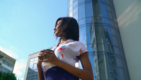 joven mujer de negocios afroamericana con café cerca de un edificio de oficinas moderno