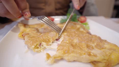 close-up of a person eating an omelet with a fork and knife