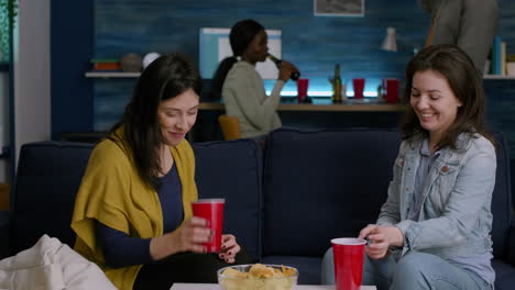 Two-women-hanging-out-at-home-party-giving-hight-five-while-relaxing-on-sofa