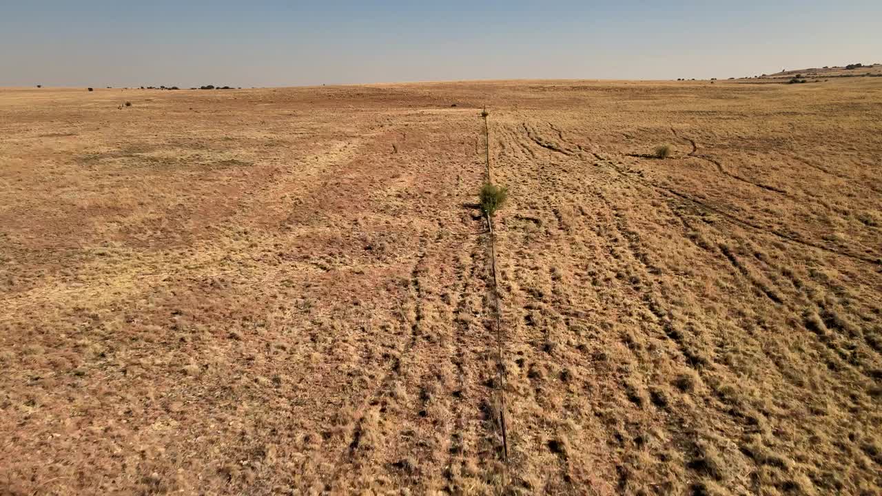 la valla de la granja desgastada, que se extiende a través del paisaje árido y árido bajo un cielo despejado - vista de un avión no tripulado de una granja remota