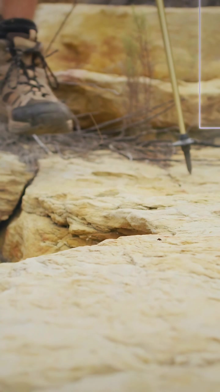 Vertical video: Male hiker planting pole, stepping on rock ledge, boot tread gripping to cross