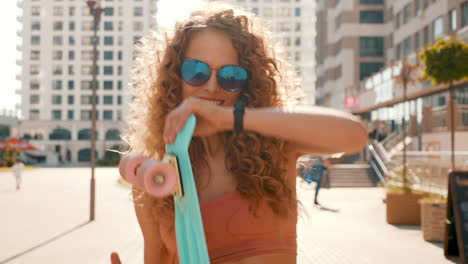 mujer con cabello rizado y gafas de sol, sosteniendo un skateboard