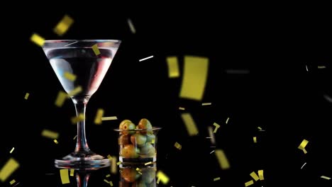 golden confetti falling over cocktail glass and olives against black background