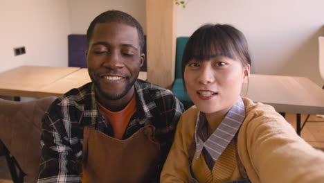 waiter and waitress taking a selfie video and talking to camera while sitting at table in coffee shop 2